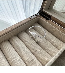 Close-up of minimalist S925 silver overlapping ring in a linen-lined wooden jewelry box