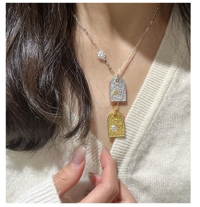 Detail of silver and gold rectangular pendants with intricate floral carvings on necklace