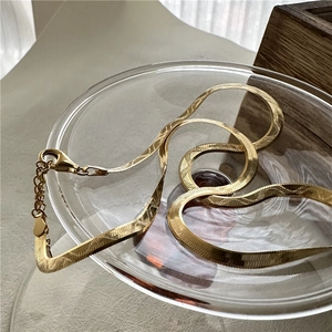 Elegant gold herringbone snake chain necklace with lobster clasp on a glass tray
