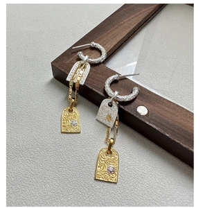 Macro detail of vintage S925 silver earrings with gold relief floral patterns on wood