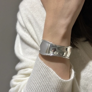 Polished silver-tone wide curved bangle bracelet with minimalist aesthetic worn on wrist