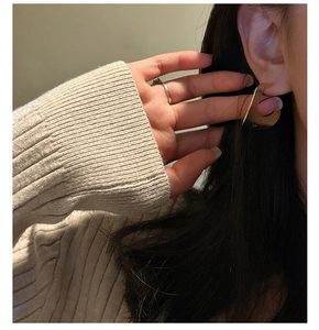 Close-up of minimalist gold matte curved earrings on model with a beige sweater