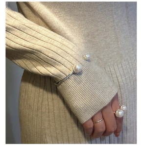Detailed view of silver minimalist bangle and double pearl ring on knit sleeve
