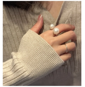 Close-up of a double pearl open ring set worn on hand with a minimalist silver band