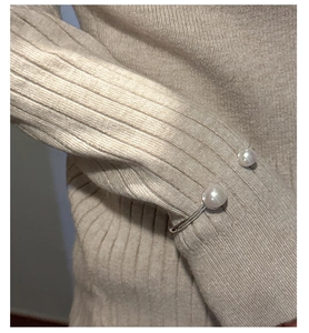 Close-up of a silver cuff bracelet with two pearls worn over a beige knit sleeve
