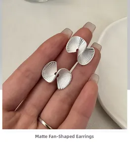 Macro detail of silver fan-shaped stud earrings with a matte brushed metallic finish