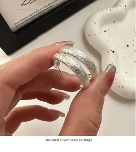 Macro shot of silver S925 brushed texture curved C-shape stud earrings with matte finish