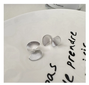 Macro view of matte S925 sterling silver fan-shaped earrings on a white ceramic tray