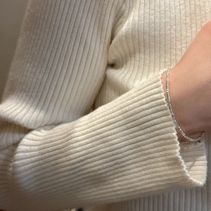 Macro shot of silver textured chain bracelet worn over a creamy knit sweater sleeve