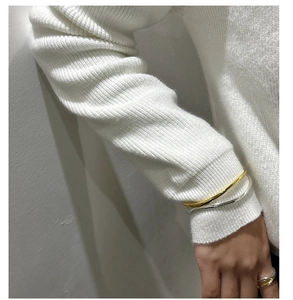 Close-up of minimalist gold and silver mixed color wavy ring worn with a white sweater