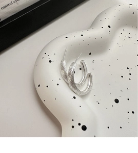 Macro view of C-shaped silver earrings with a brushed matte texture on a white tray