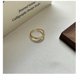 Detailed view of dual-layer overlapping S925 silver and gold wave ring on textured background