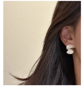 Macro detail of silver fan-shaped earring with spiral matte texture on model's ear