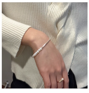 Detail showing a minimalist pearl bracelet and gold ring set worn on a beige sweater
