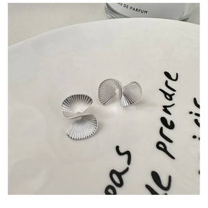 Macro detail of matte S925 sterling silver fan-shaped spiral earrings on ceramic tray