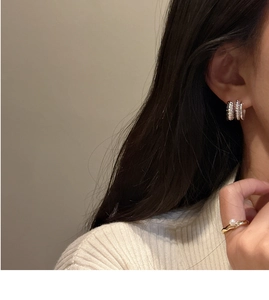 Détail de boucles d'oreilles torsadées en argent et bague perle sur modèle au style élégant