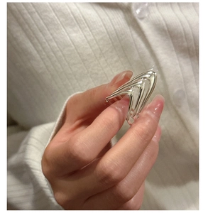 Close-up of a layered geometric silver ring being held against a white knit background