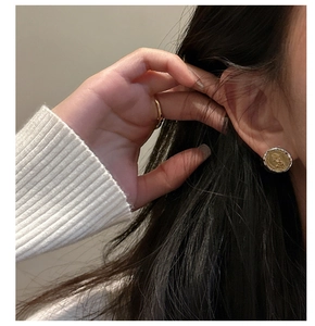 Detail view of retro S925 silver coin stud earring and gold ring on female model