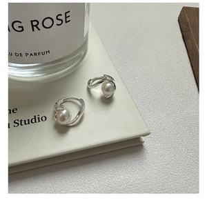 Détail des créoles torsadées en argent avec perles blanches élégantes sur un fond délicat