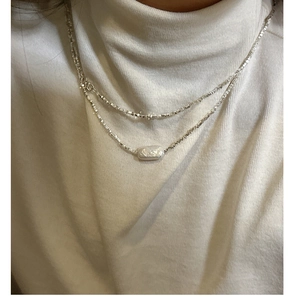 Detail of layered S925 silver necklace with irregular pearl pendant on a model