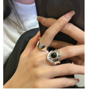 Close-up of a wide silver band stacked with an oval black onyx ring on a finger