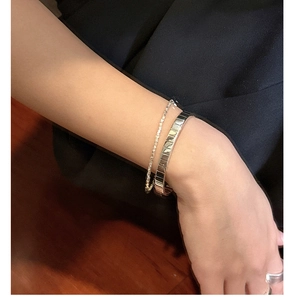 Close-up of a S925 sterling silver textured gear bangle and a dainty sparkling chain bracelet