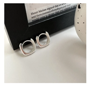 Gros plan de boucles d'oreilles créoles carrées en argent poli sur fond artistique