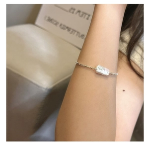 Macro view of a rectangular baroque pearl on a fine silver chain bracelet worn on wrist
