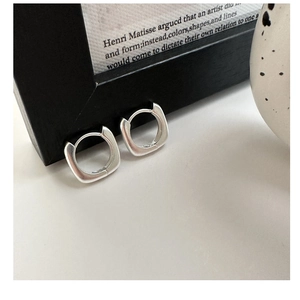 Détail macro de créoles carrées en argent avec finition mate brossée sur fond sombre