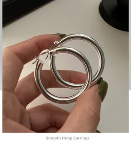 Close-up of large polished silver hoop earrings held to show scale and smooth finish