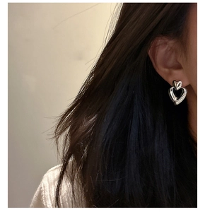 Close-up of a model wearing double-layered silver heart stud earrings with a polished finish