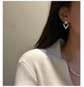 Close-up of a model wearing silver double heart drop earrings with a pearl necklace