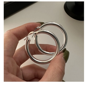 Detailed view of large S925 sterling silver hoop earrings held by hand for size reference