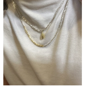 Detail of layered S925 silver and gold necklace with water drop pendant on a model