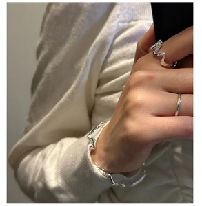 Vue détaillée de bagues et bracelet argentés ondulés minimalistes portés sur mannequin