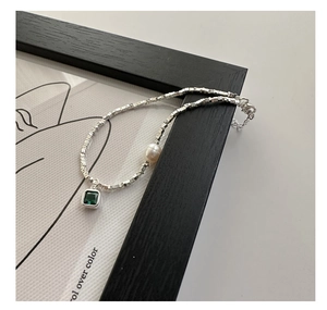 Détail macro d'un collier en perles d'argent S925 avec zircon vert et perle blanche