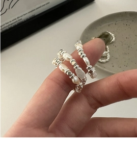 Gros plan de bagues en perles baroques et perles d'argent portées en superposition
