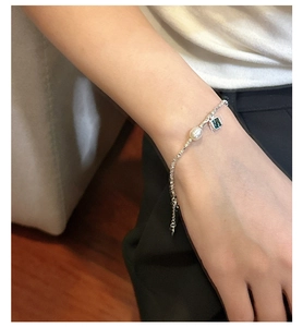 Détail du bracelet en argent avec pendentif en zircon vert et perle au poignet féminin