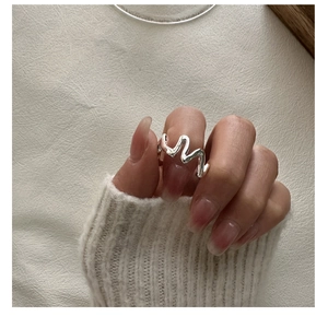 Gros plan d'une bague ondulée en argent sterling S925 aux courbes polies sur un doigt