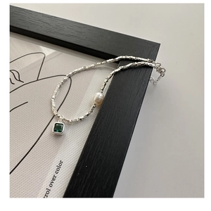 Gros plan d'une chaîne en argent S925 avec zircon vert et perle sur une carte d'art