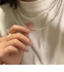 Close-up of S925 silver pearl necklace and rings worn over white knitted fabric