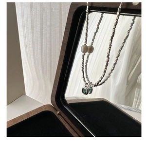 Detail of silver box-chain necklace with a white pearl and green gemstone pendant
