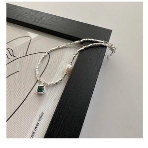 Detail of silver chain with emerald gemstone and pearl pendant on black frame