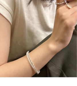 Detail view of double-layer silver pearl necklace and matching rings on a female model