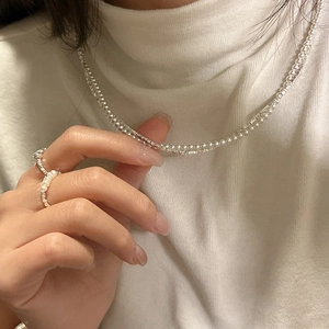 Double-layer S925 silver necklace with pearls and matching rings on a white knit sweater