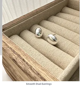 Macro shot of smooth silver oval stud earrings in a wooden jewelry box display