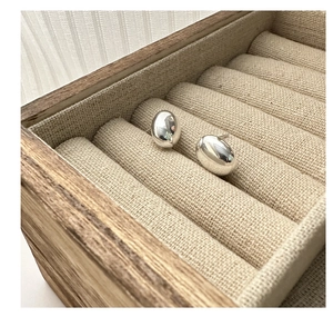 Macro shot of polished S925 silver bean studs on a natural linen jewelry box display