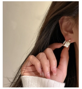 Detail of square silver earring with 22 relief on a model wearing white knitwear
