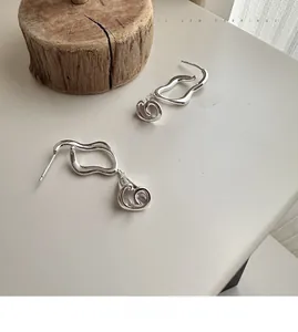 Detail view of S925 silver calla lily earrings with polished wavy design on wood base