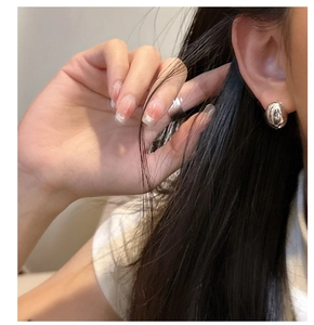 Close-up of a model wearing polished S925 sterling silver oval stud earrings in a warm light